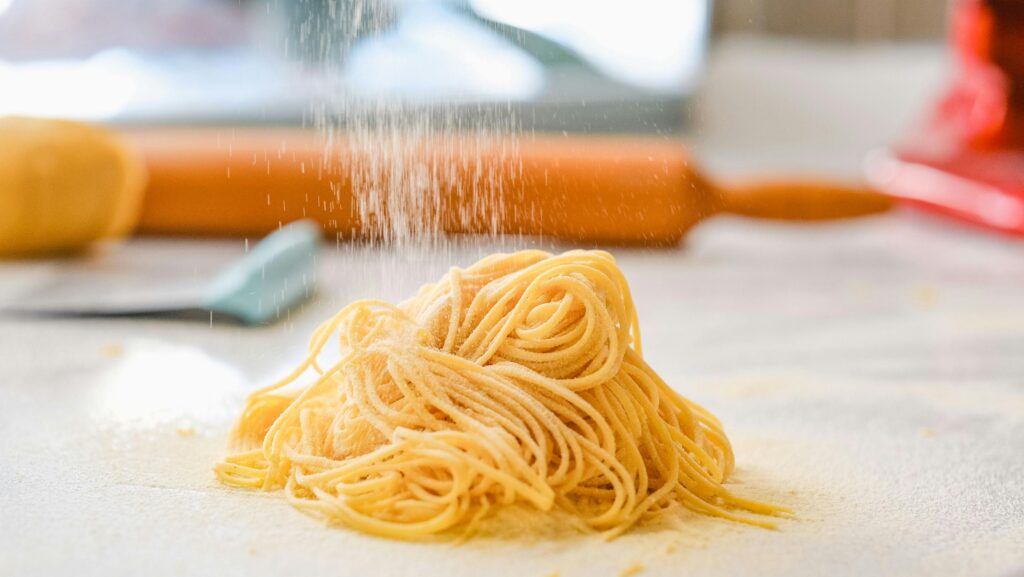 Close-up of homemade pasta being sprinkled with flour indoors.